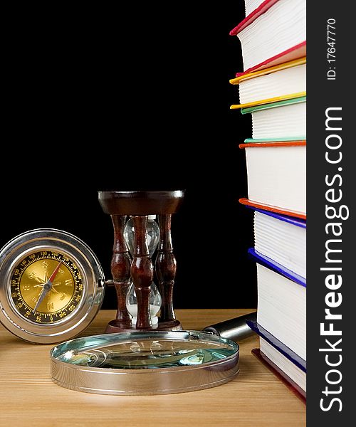 Pile of books, compass and hourglass on black background