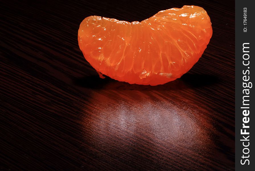 A peeled Tangerine segment on a dark brown wood table. A peeled Tangerine segment on a dark brown wood table