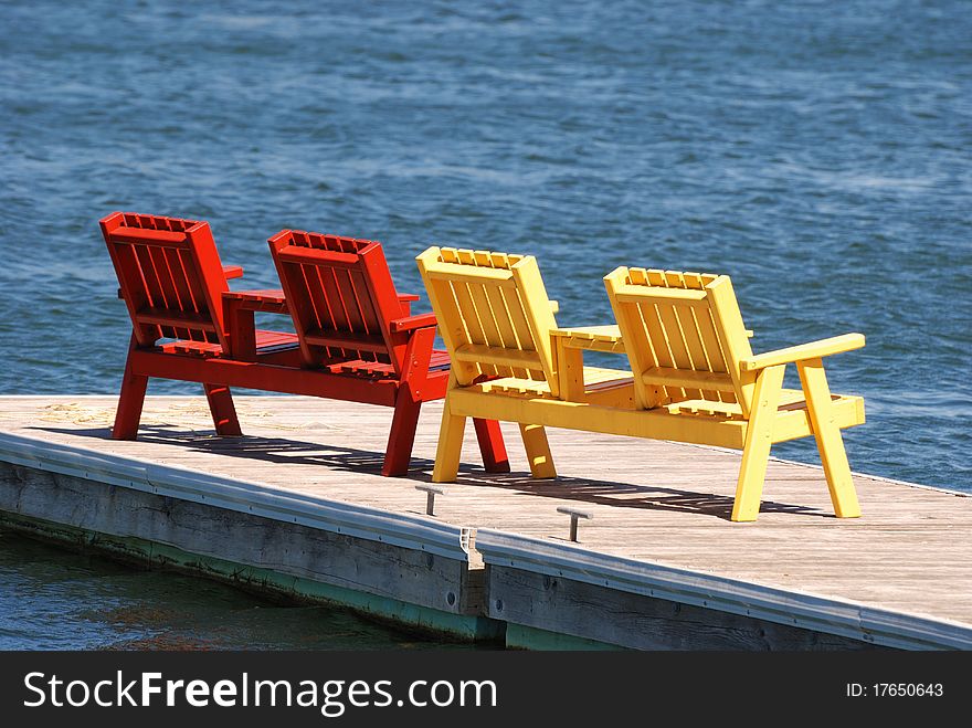 Two pairs of colorful chairs sit on a dock.