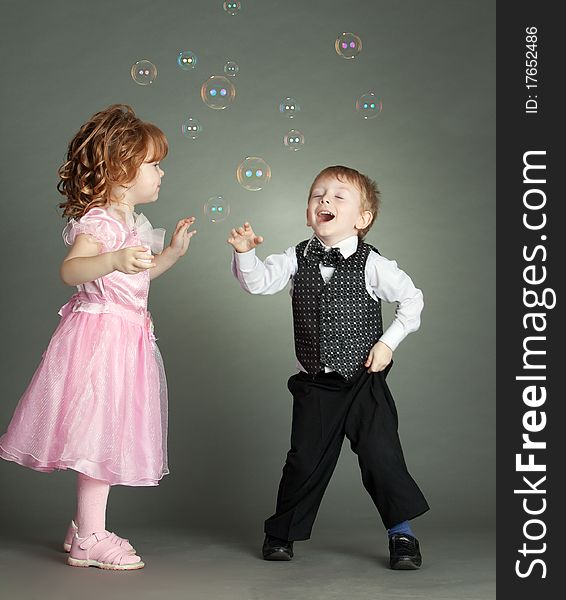 The boy and the girl cheerfully play with soap bubbles. The boy and the girl cheerfully play with soap bubbles