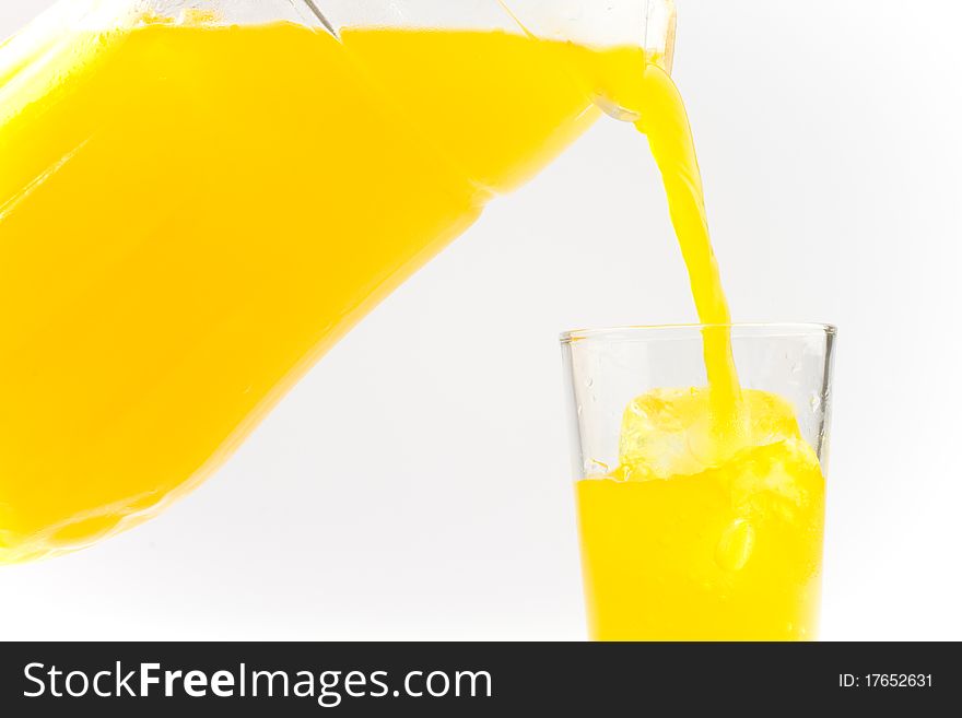 Orange cold drink poured from a glass container into a glass filled with ice. Orange cold drink poured from a glass container into a glass filled with ice