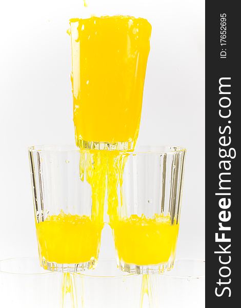 Chilled yellow orange cold drink poured splashing in a stack pyramid of cold glasses filled with ice. Chilled yellow orange cold drink poured splashing in a stack pyramid of cold glasses filled with ice