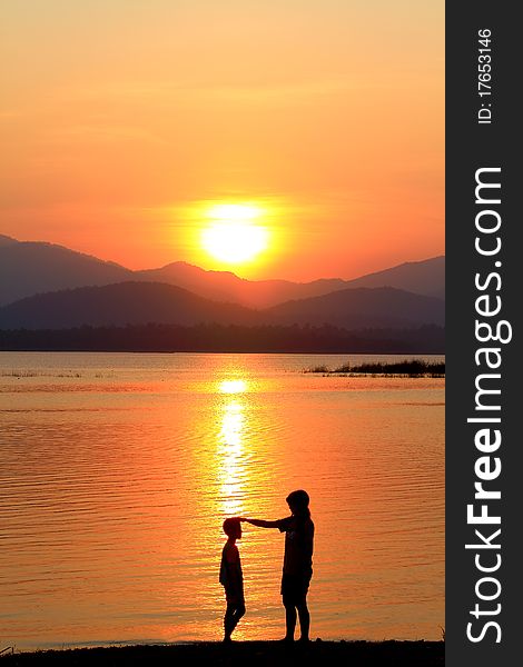 A mother and daughter stand silhouetted against a cloudy sunset sky on the beach. A mother and daughter stand silhouetted against a cloudy sunset sky on the beach