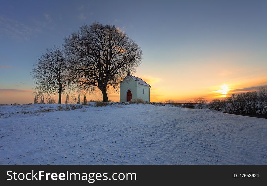 Sunset on frozen field with a chapel and clouds