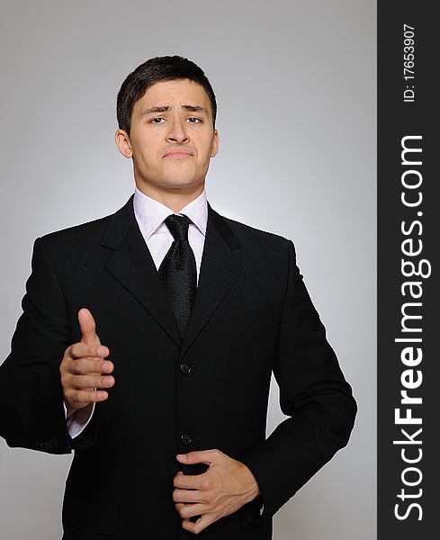 Young serious business man in black suit and tie. gray background