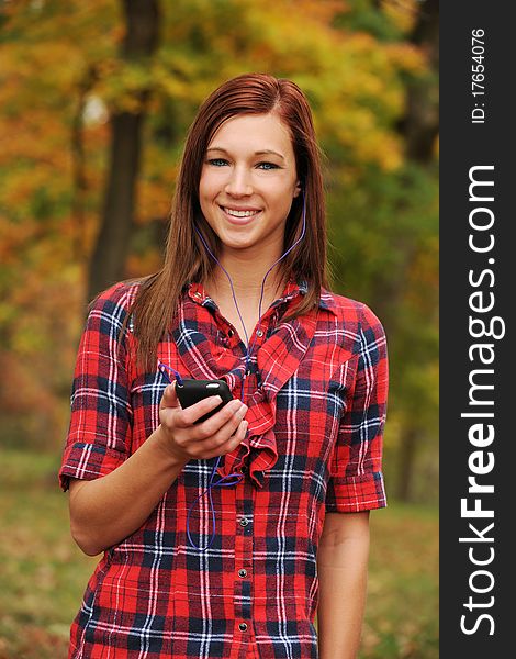 Young Woman listening to music with headphones and fall bacground out of focus