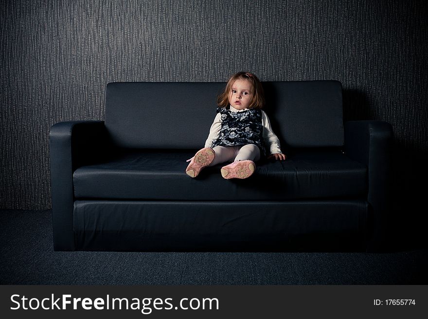 Little girl sitting on black sofa. Little girl sitting on black sofa