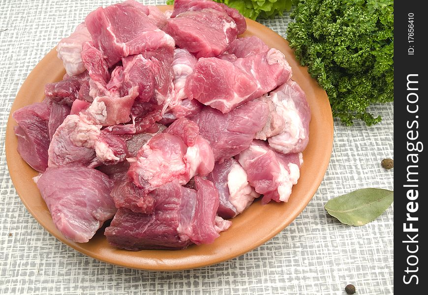 Meat cut by large pieces is in a plate on a kitchen table. Meat cut by large pieces is in a plate on a kitchen table