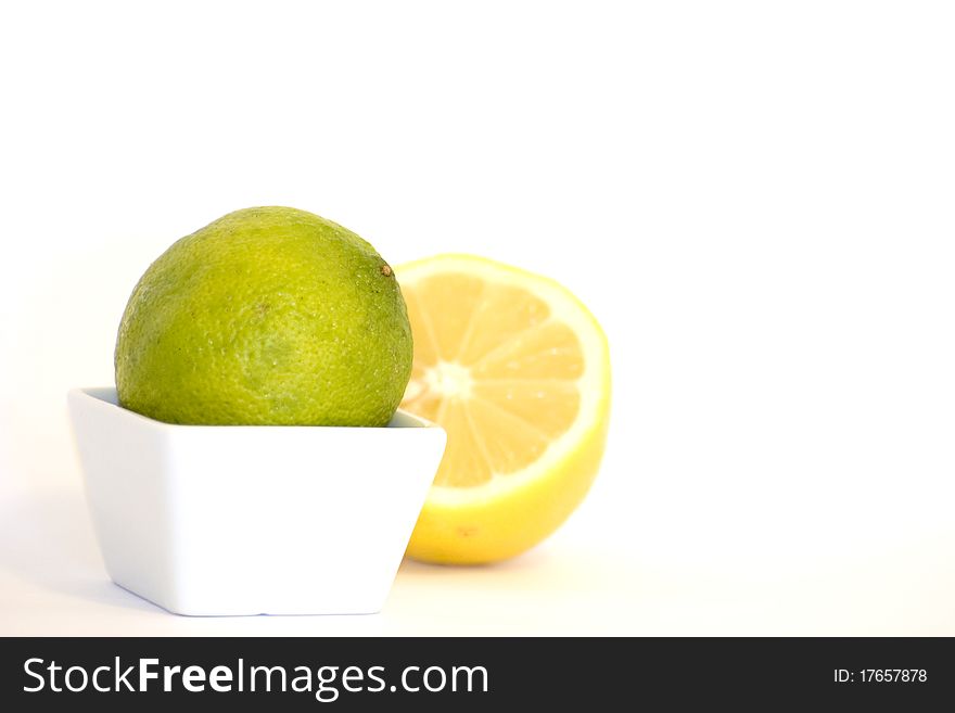 A close up of a lime in a small recipient and a cut lemon in the back. A close up of a lime in a small recipient and a cut lemon in the back.