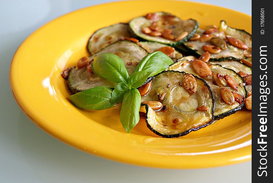Fried courgette snack with pumpkin seeds in yellow plate decorated with basil