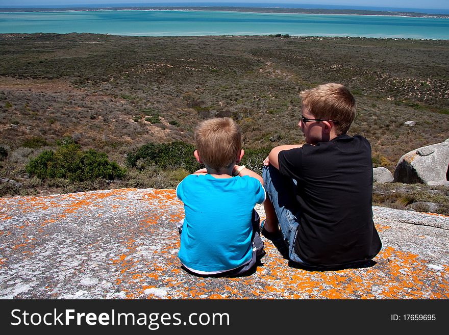 Brothers on vacation sitting on rock looking out over Langebaan lagoon in the westcoast national park in south africa. Brothers on vacation sitting on rock looking out over Langebaan lagoon in the westcoast national park in south africa