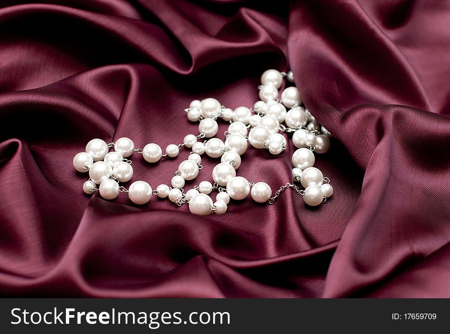 Shiny white pearls on ruby satin background