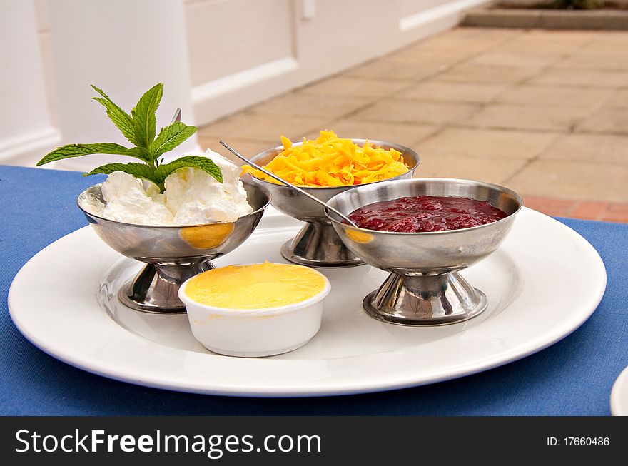 Condiments of cheese, cream, strawberry jam served with sconce in silver bowls on white plate in restaurant. Condiments of cheese, cream, strawberry jam served with sconce in silver bowls on white plate in restaurant