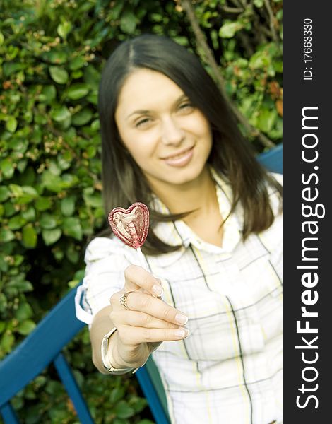 Young woman in an outdoors holding a lollipop in the shape of the heart. Sad. Young woman in an outdoors holding a lollipop in the shape of the heart. Sad