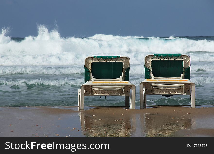 Beach loungers on the background of the sea storm. End of the season, winter.