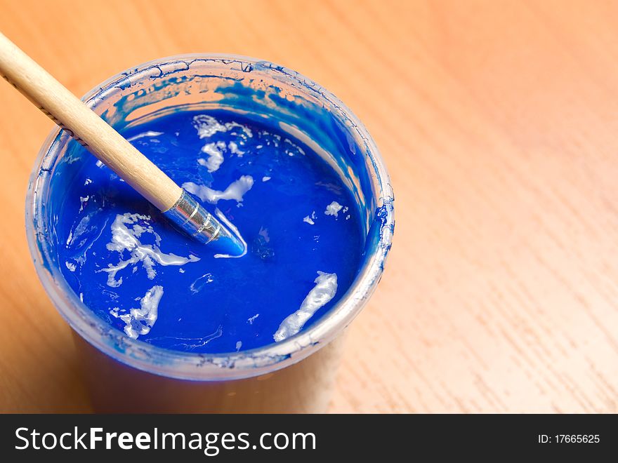 Jar with a blue paint and a brush on a wooden background