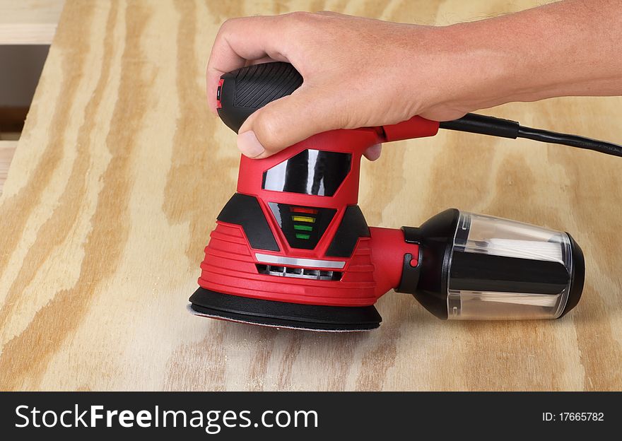 Electric circular sander sanding a piece of plywood. Electric circular sander sanding a piece of plywood