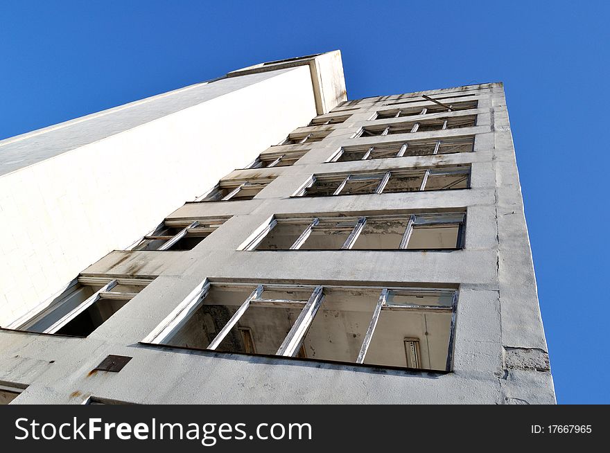 Damaged old grunge industrial building with broken windows upon blue sky