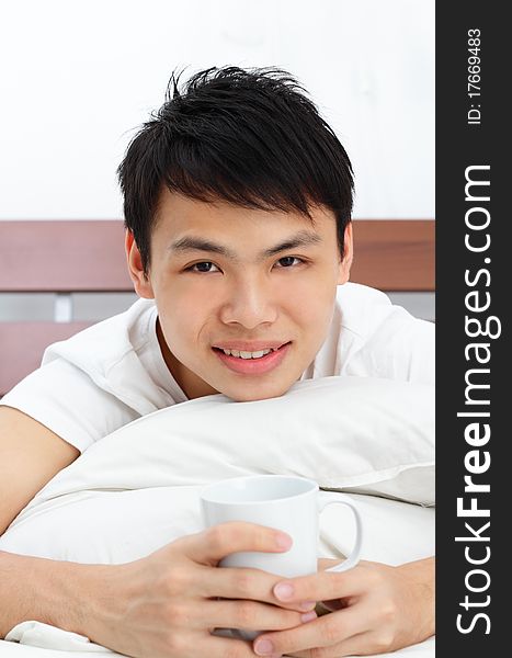 An Asian man having some coffee in bed. An Asian man having some coffee in bed