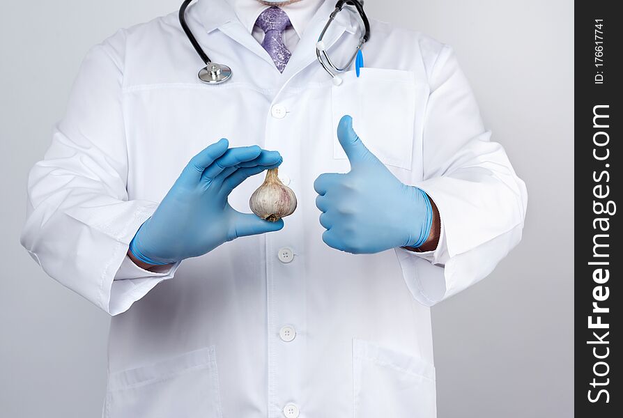 Doctor in a white medical coat and blue rubber gloves holds a fresh head of garlic, prevention against viral diseases, traditional medicine