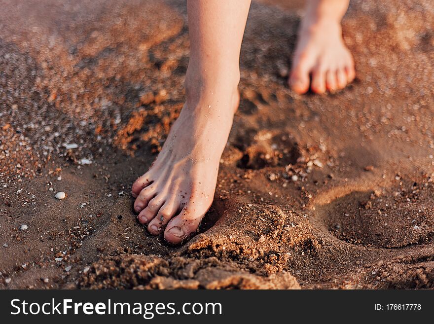 Women`s Feet Walk On The Sand On The Beach