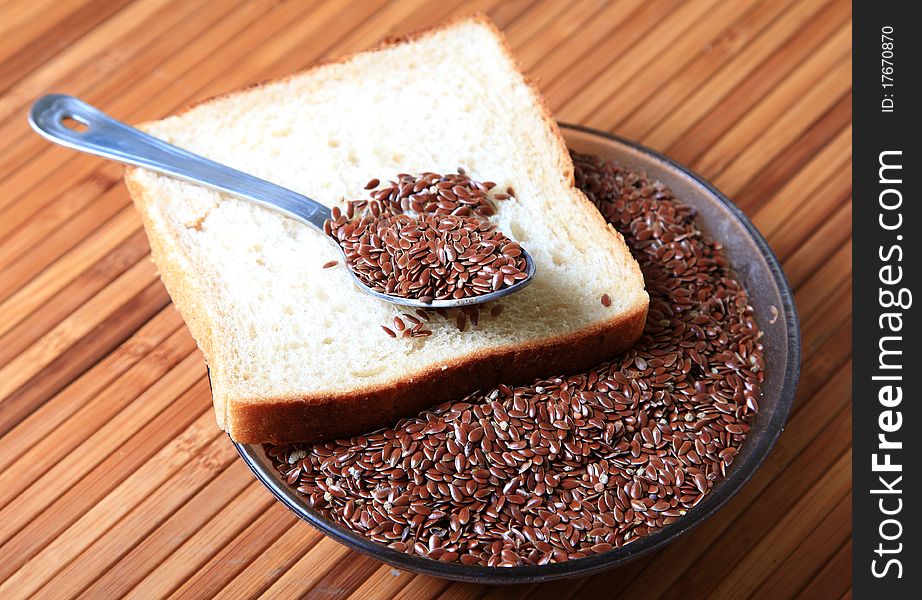 Closeup shot of bowl of raw linseed's with brown bread slice over wooden background. Closeup shot of bowl of raw linseed's with brown bread slice over wooden background.