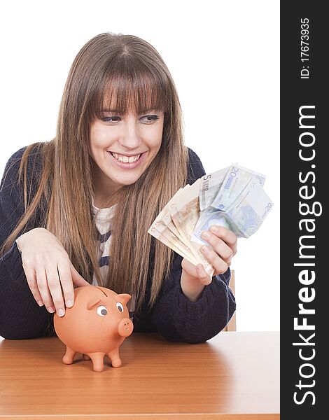 A young woman holding euro notes with a pig bank on the table. A young woman holding euro notes with a pig bank on the table