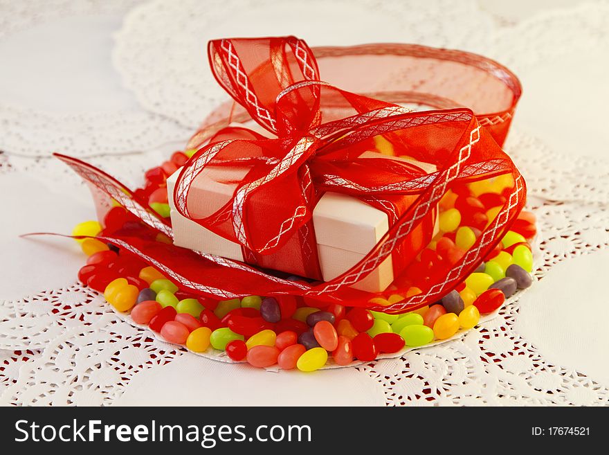 White package wrapped in red ribbon placed on colorful jellybeans and paper doilies. White package wrapped in red ribbon placed on colorful jellybeans and paper doilies