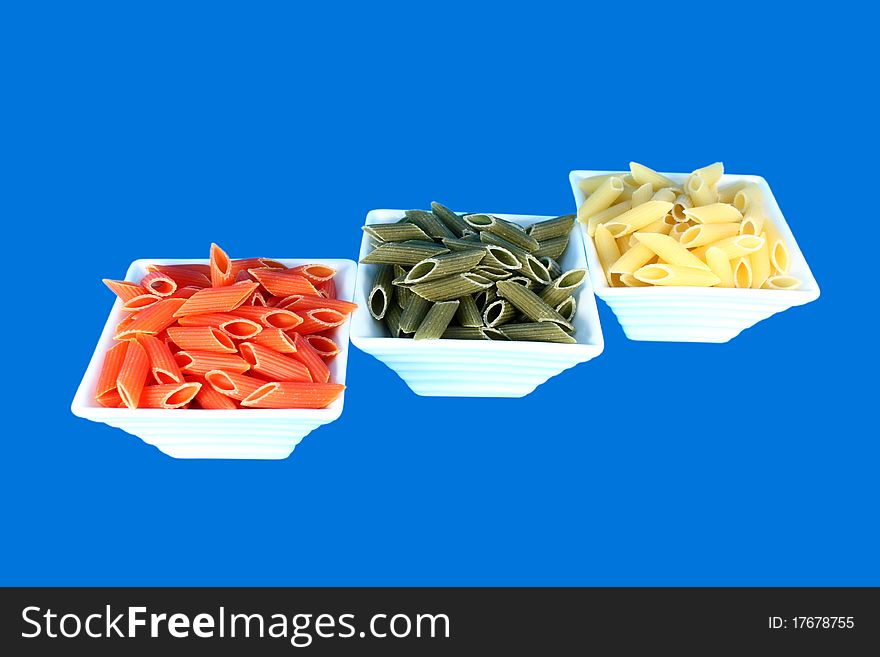 Three white bowls ful of colorful pasta isolated on blue