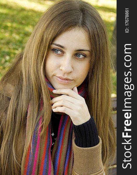 Vertical portrait of a beautiful young woman sitting on a bench in the park around a lot of yellow, red green leaves, looks into the camera. Vertical portrait of a beautiful young woman sitting on a bench in the park around a lot of yellow, red green leaves, looks into the camera.