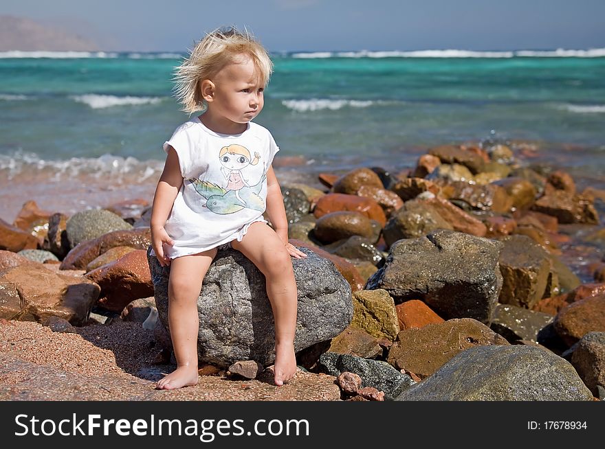 Little girl sitting on the stones at the beach. Little girl sitting on the stones at the beach