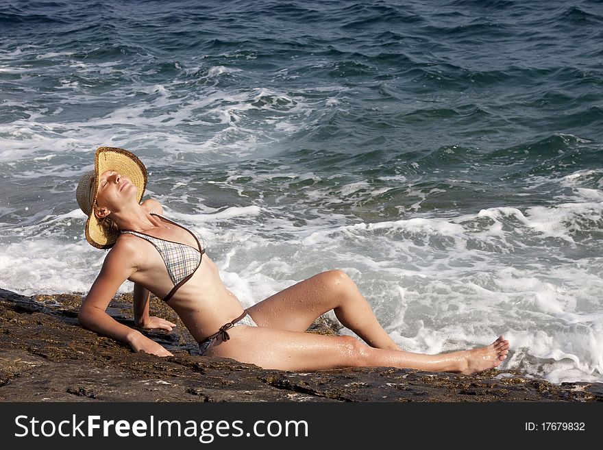 Woman with hat sitting on rocks near big waves