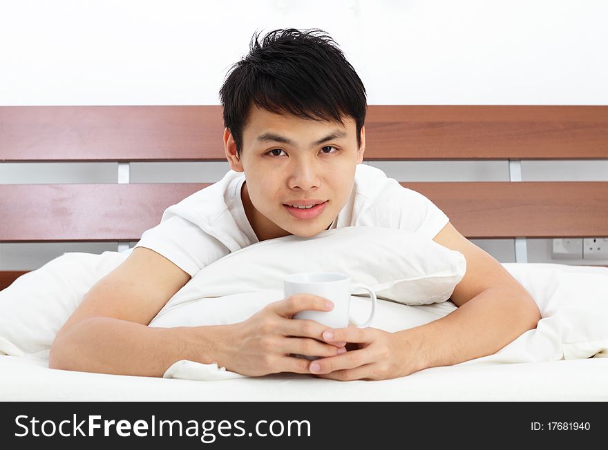 An Asian man drinking coffee in bed. An Asian man drinking coffee in bed