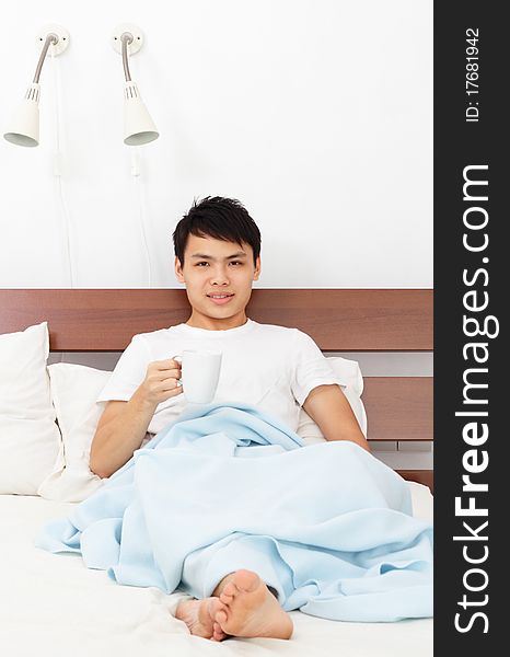 An Asian man with a coffee mug in bed. An Asian man with a coffee mug in bed