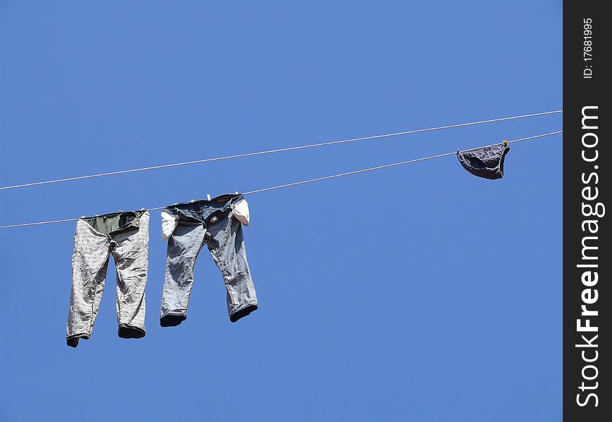 Jeans, trousers and men's swimming trunks are dried on the line against the blue sky. Jeans, trousers and men's swimming trunks are dried on the line against the blue sky