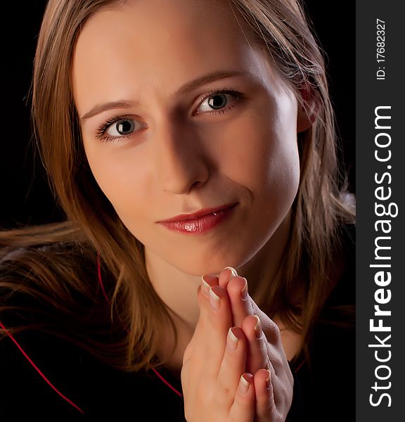 Beautiful young woman with hands folded asking for help on black background