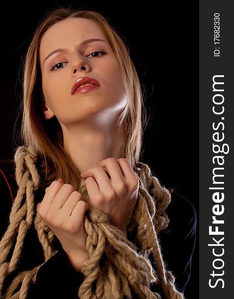 Seductive young woman tied in ropes on black background