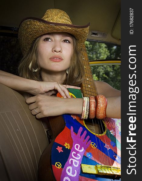 Beautiful young girl sitting in the car with a guitar