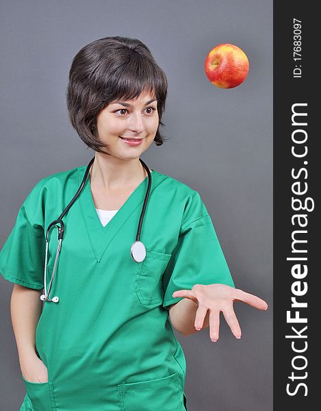 Attractive lady doctor with fresh apple on gray background