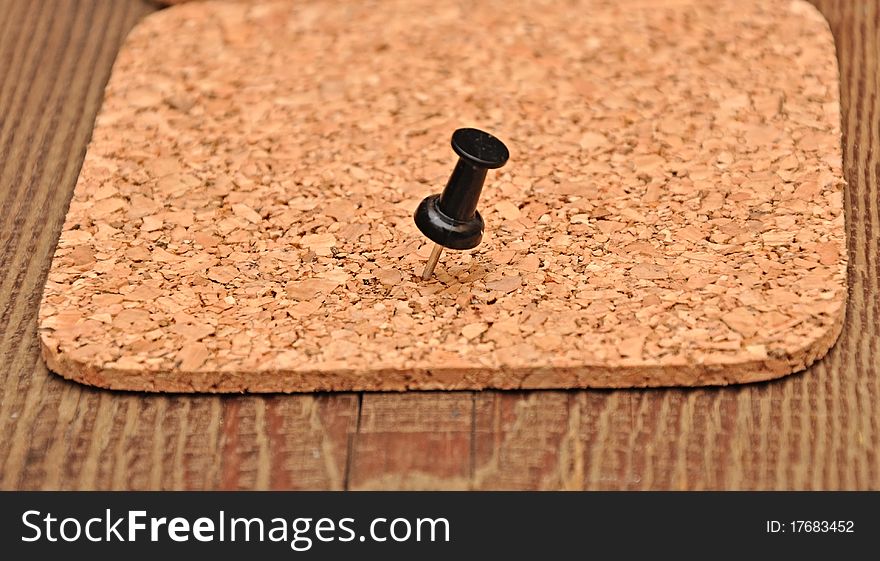Cork texture pressed black pushpin on wood background