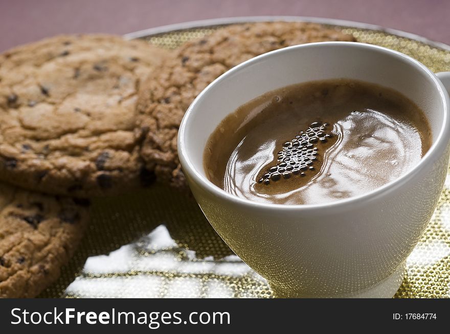 Coffee cup and chocolate cookies on a plate over color background