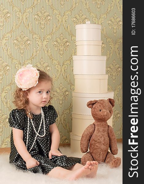 Little girl dressed as a retro doll sits on the floor with a toy