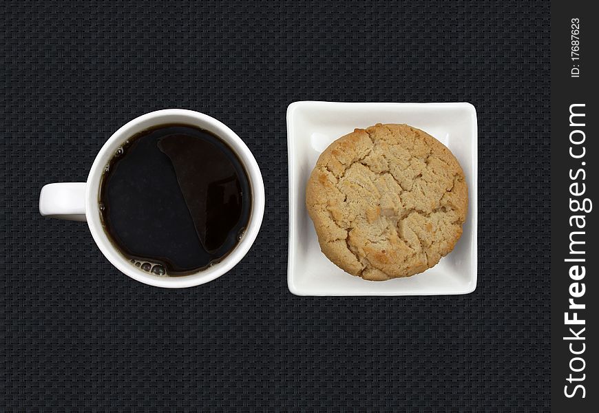 Cup of black coffee and a peanut butter cookie on black. Cup of black coffee and a peanut butter cookie on black