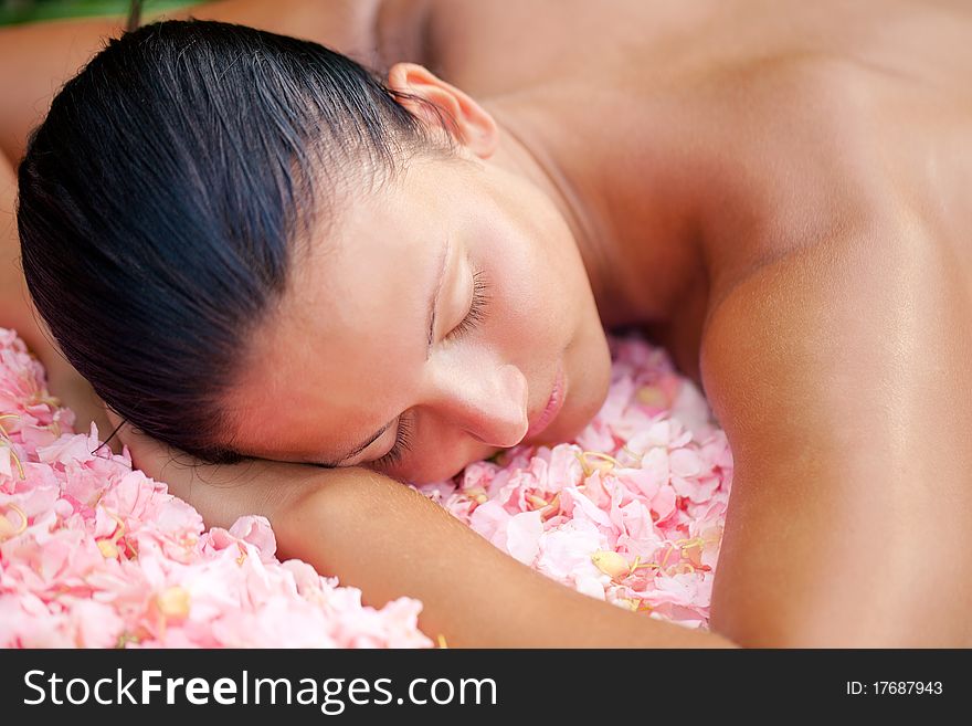 Beautiful woman relaxing on the massage table covered by flowers