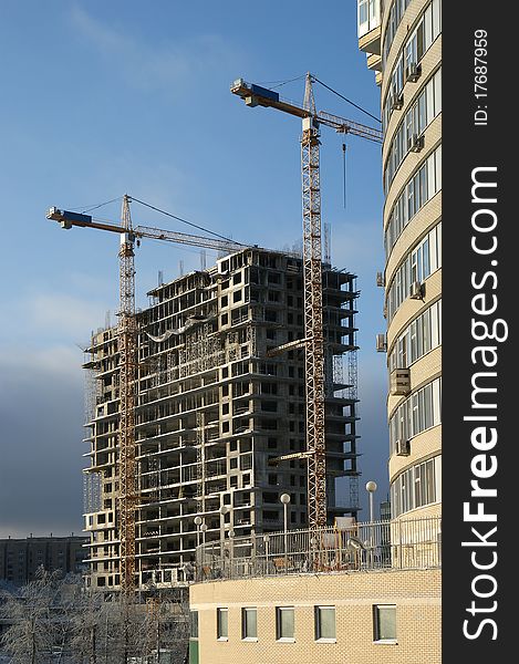 Elevating construction crane and building under construction on the blue clear sky