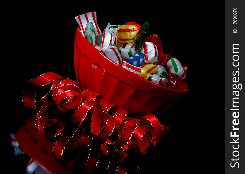 REd bowl of christmas candy, angled and reflecting in a black shiny surface. REd bowl of christmas candy, angled and reflecting in a black shiny surface