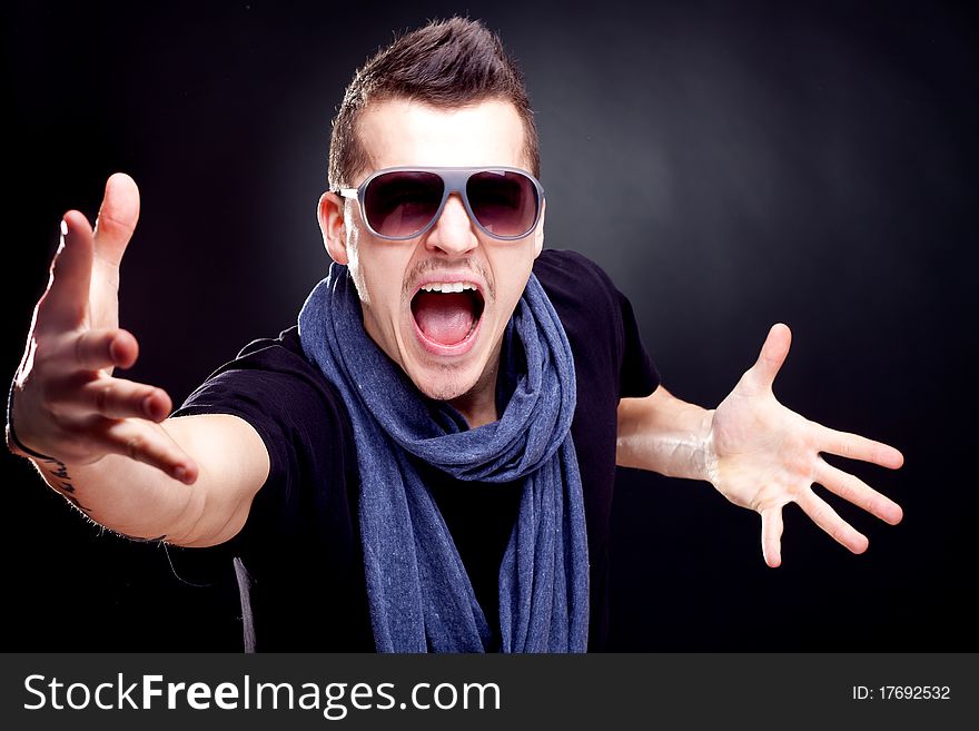 Fashion man wearing a blue scarf and sunglasses screaming on a dark background. Fashion man wearing a blue scarf and sunglasses screaming on a dark background