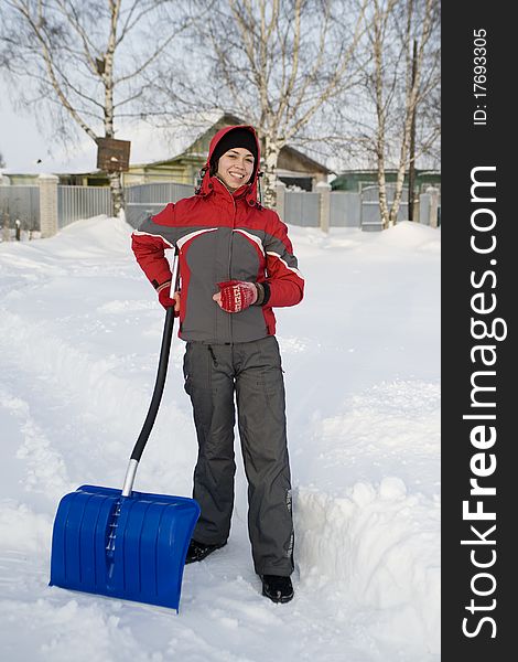 The girl in a winter sports jacket holds a shovel for cleaning of snow and smiles