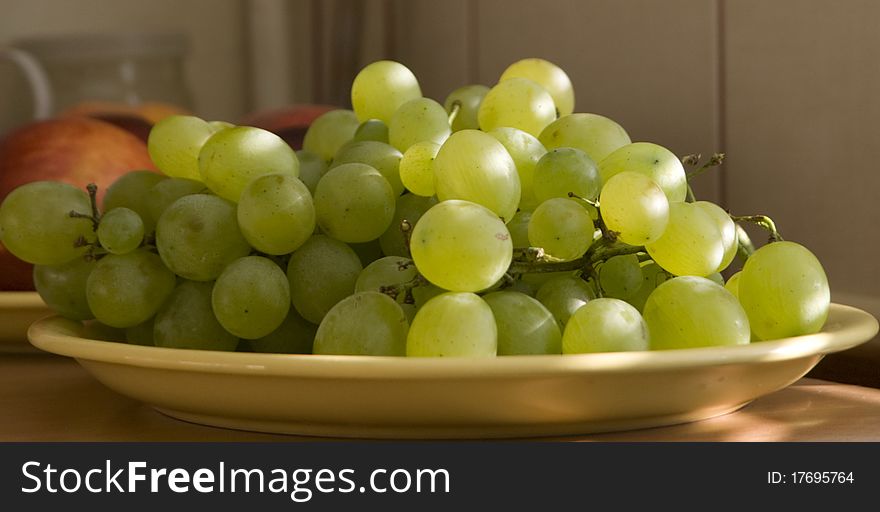 Still life with white grapes on a yellow plate in the sun