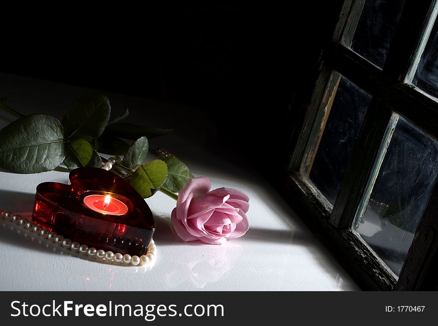 Pink rose and heart shaped candle lit by window light. Pink rose and heart shaped candle lit by window light